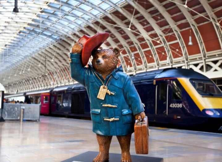 A statue of Paddington standing in the middle of a train station.