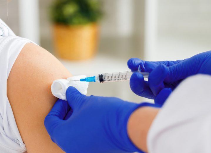 A doctor wearing dark blue gloves injecting a person's shoulder with a needle.