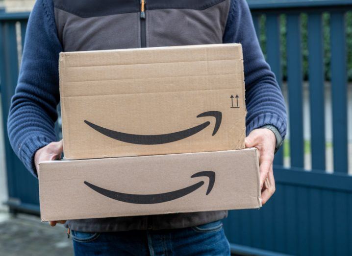 A person holding two cardboard boxes which have the Amazon Prime logo on them, with a dark gate in the background.