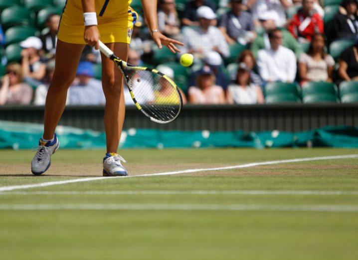 A close-up of a tennis player holding a ball, about to serve on a grass tennis court.