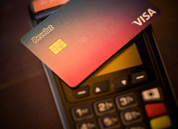 A Visa card with the Revolut logo, resting on a card reader that is on a brown table background.