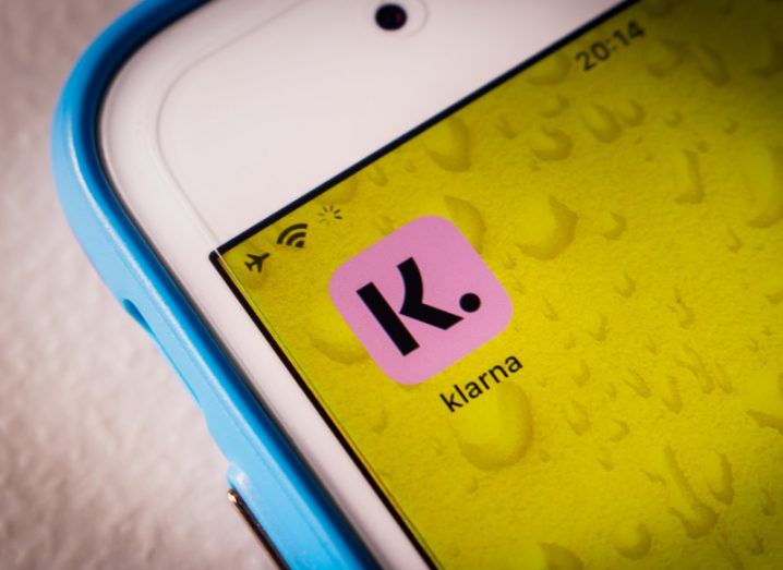 Close-up of a smartphone with the Klarna app on its screen on a yellow background.