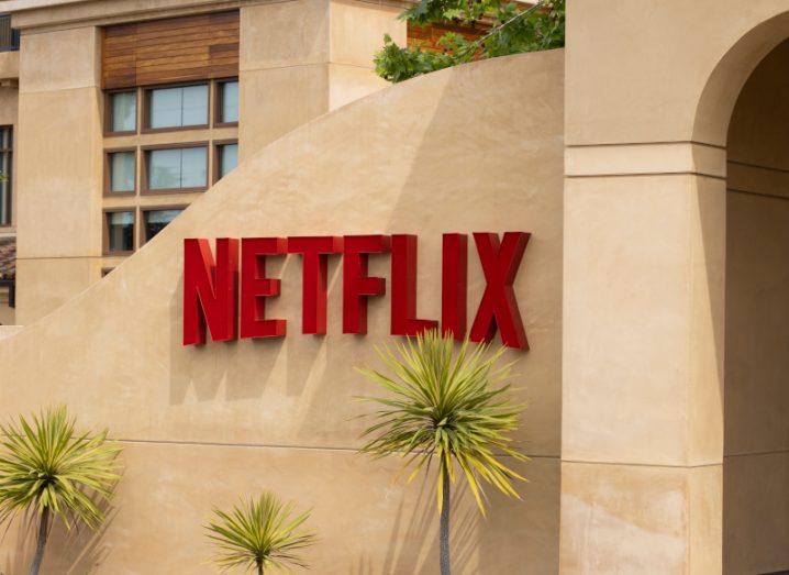 Netflix logo on the side of a tan wall with small trees under it.