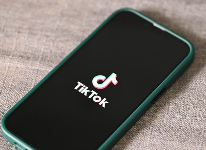 Mobile phone with the Tiktok logo on the screen. The phone is resting on brown material.