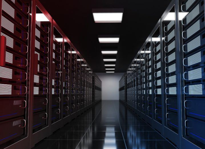 Hallway of a data centre with lights on the ceiling. The servers are red on the left and blue on the right.