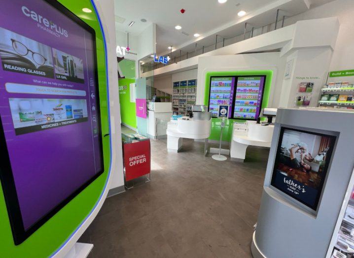 Interior of a pharmacy with screens visible on the side and in the background of the image. It is CarePlus Pharmacy in Drumcondra.