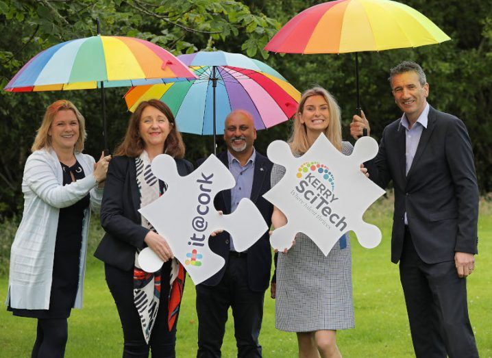 Five people standing outside holding three umbrellas and two giant jigsaw puzzle signs with IT@Cork and KerrySciTech branding.