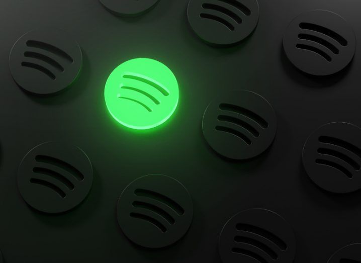 Spotify logo glowing in neon green among many other Spotify logos in the dark.