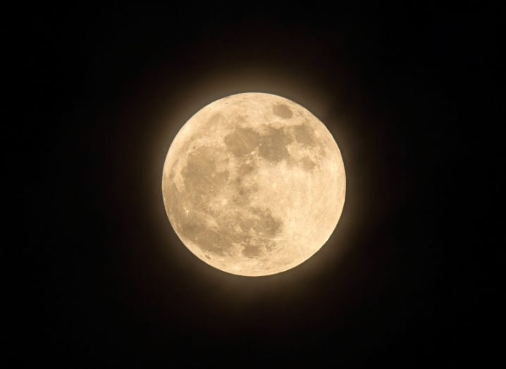 A big and bight supermoon with a yellowish hue in a pitch black night sky background.