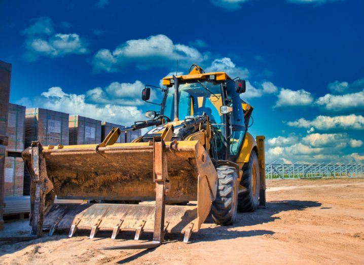 A bulldozer parked in the sun with solar panels visible in the distance.