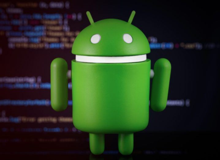 Google Android logo in 3D with code displayed on a screen in the background.