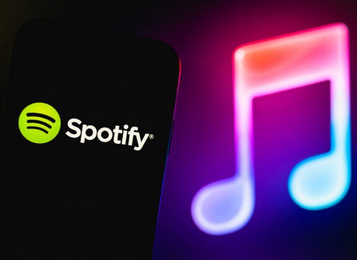 Spotify logo on a smartphone with a glowing neon-coloured musical note symbol in the background.