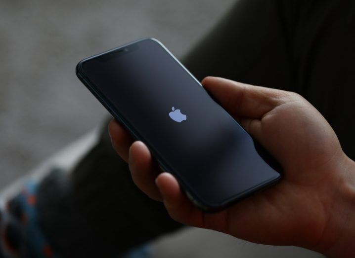 Image of a person's hand holding an iPhone with the Apple logo displayed on screen.