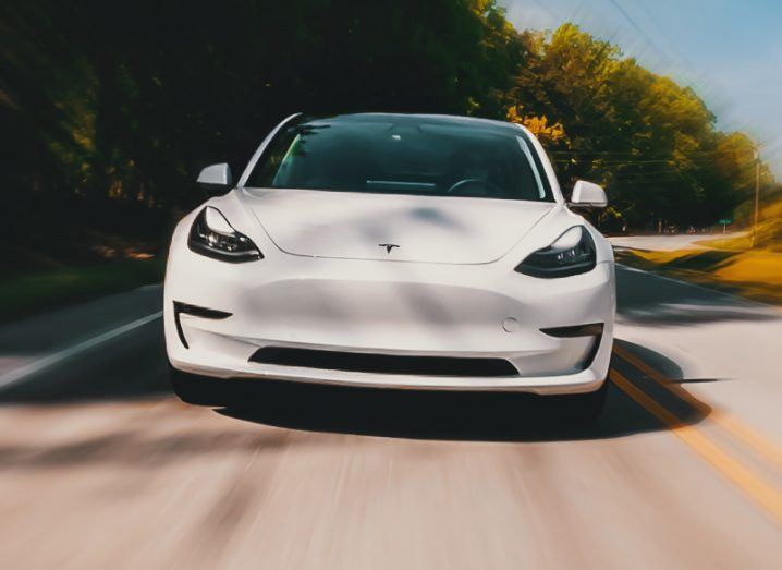 A white Tesla EV in motion on the road.