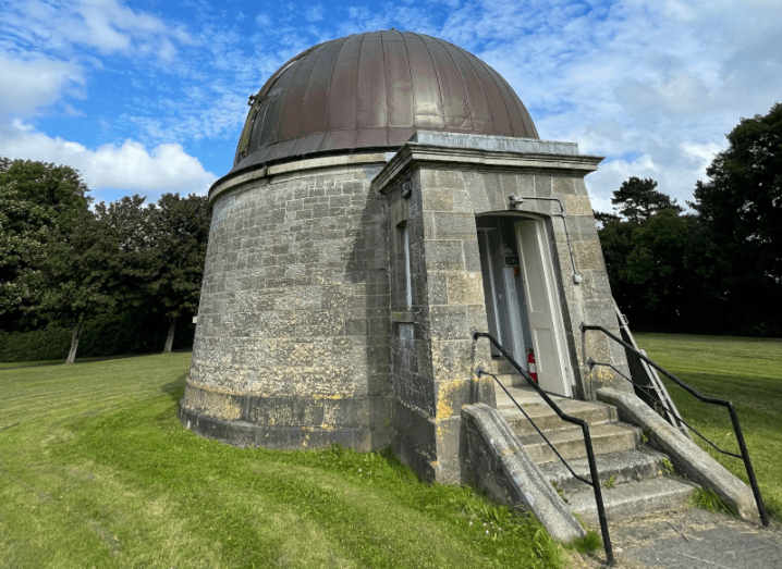 A domed building with stairs leading into it on a green field.
