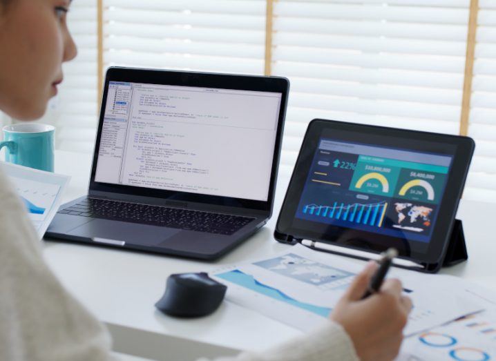 A woman working on two screens showing lines of code and various graphs, symbolising data management.