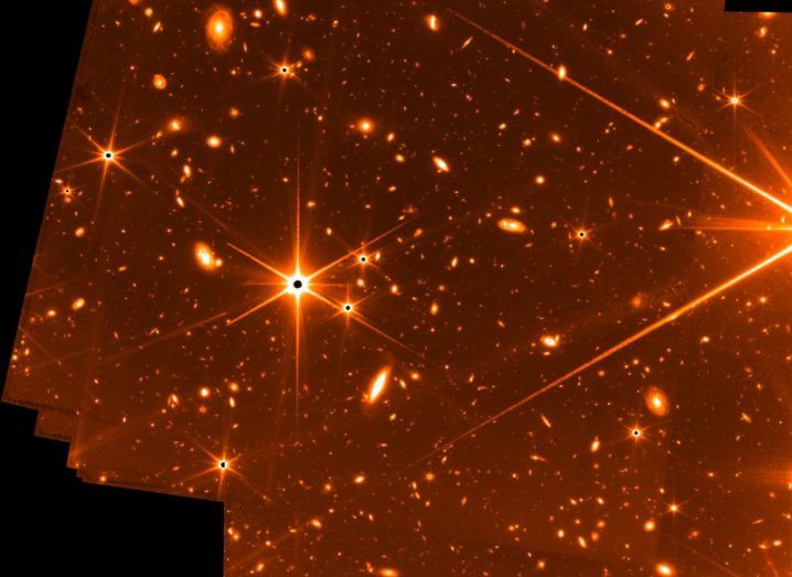 Orange image showing distant stars and galaxies, with some black edges. The image came from the James Webb Space Telescope.