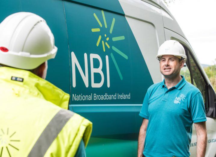 Two workers in hard hats stand beside a van with the National Broadband Ireland logo on the side.