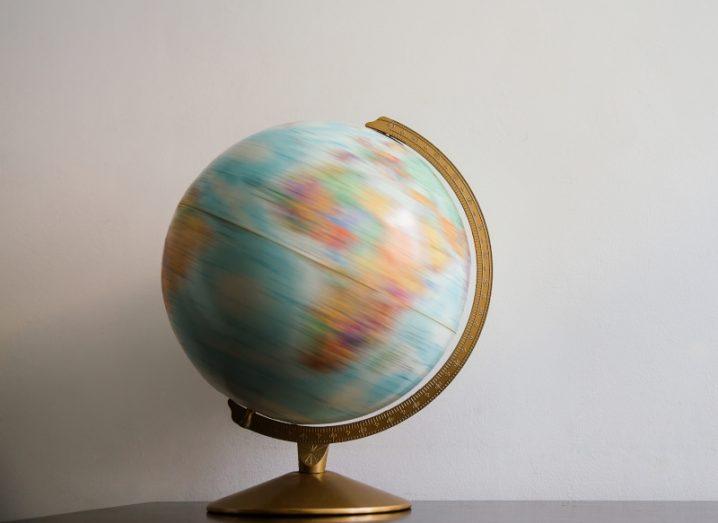 A globe of the Earth spinning while resting on a table, with a white wall in the background.