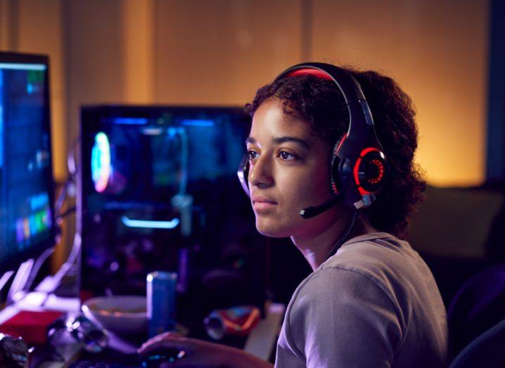 A person with a headset and microphone looking at desktop monitors and playing a game.