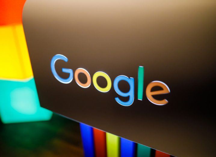 The Google logo on a black surface with a wooden floor and different coloured lights visible in the background.