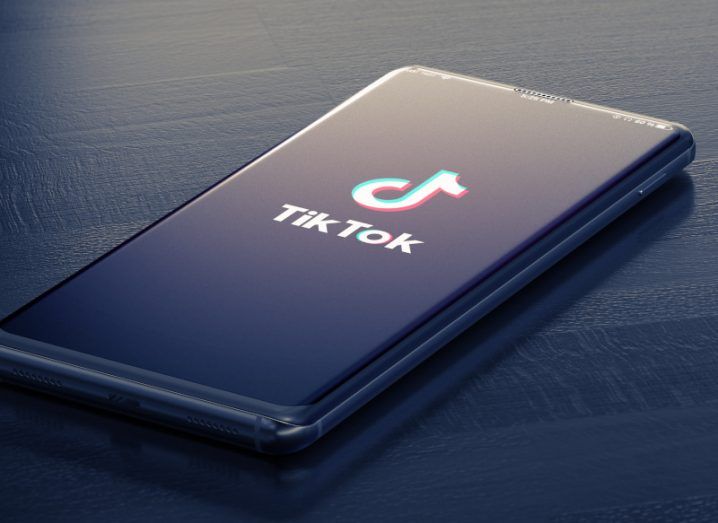A mobile phone with the TikTok logo on the screen, laying on a dark wooden table.