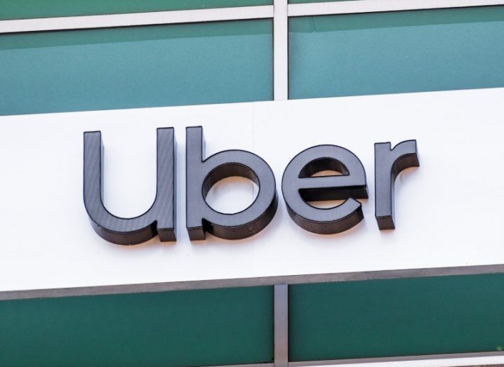 A grey Uber logo on a white and green building wall.