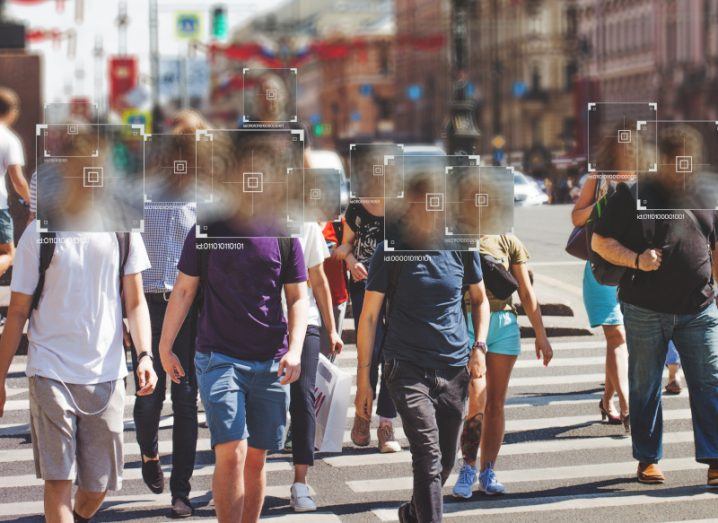A group of people walking across a road, with their faces blurred with squares. Used to represent facial recognition technology.
