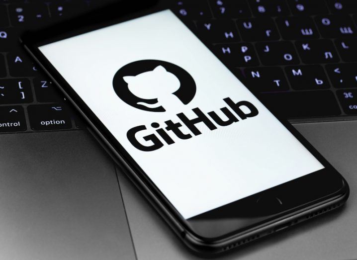 A mobile phone with the GitHub logo on the screen, laying on a laptop keyboard.