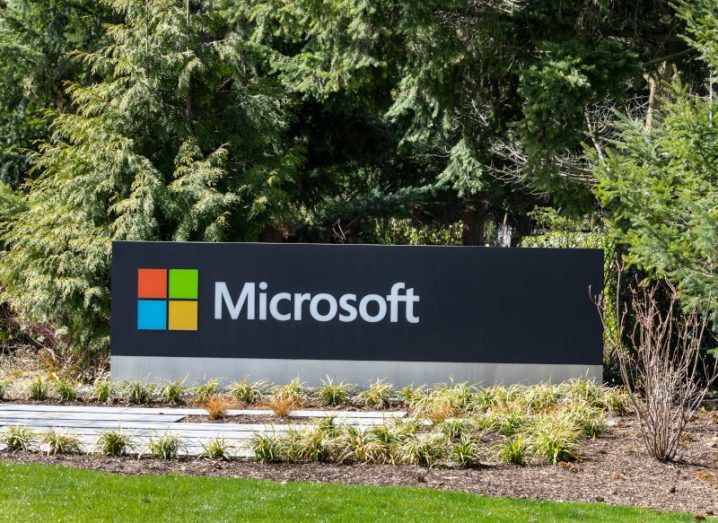 A black sign with the Microsoft logo on it, with trees behind it and grass in front.