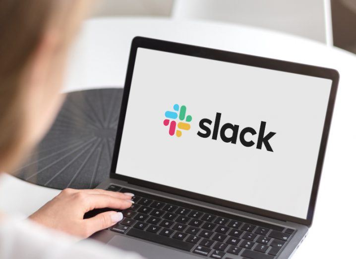 A person using a laptop with the Slack logo on the screen, resting on a white table.