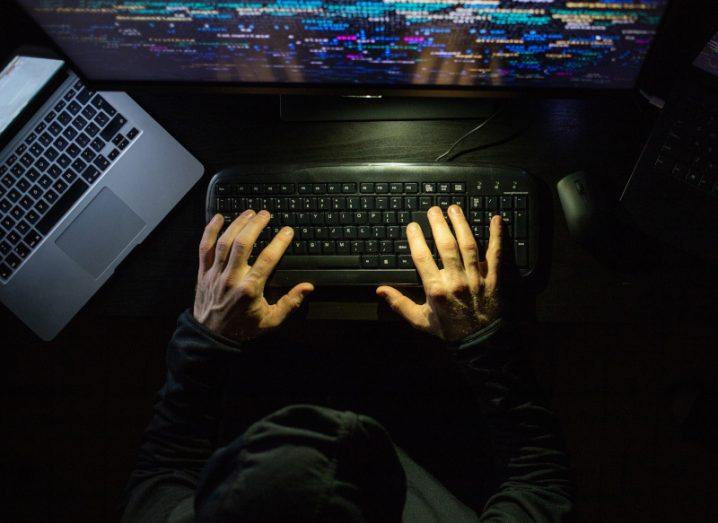 A person wearing a dark outfit typing code onto a computer.
