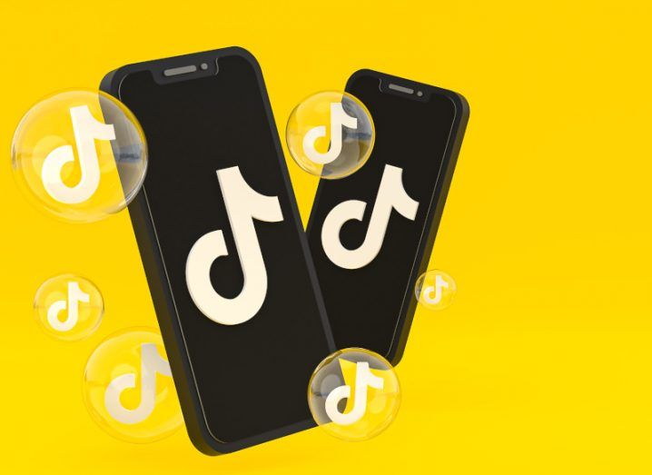 Two smartphones with the TikTok logo on their screens sit against a bright yellow background with transparent bubbles also featuring the TikTok logo on them.