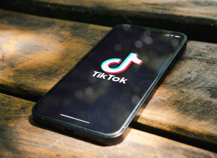 Mobile phone with the TikTok logo on the screen, laying on a wooden floor.
