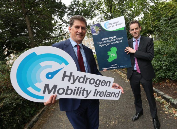 Two men in suits pictured in a park, holding up signs that say 'Hydrogen Mobility Ireland'.