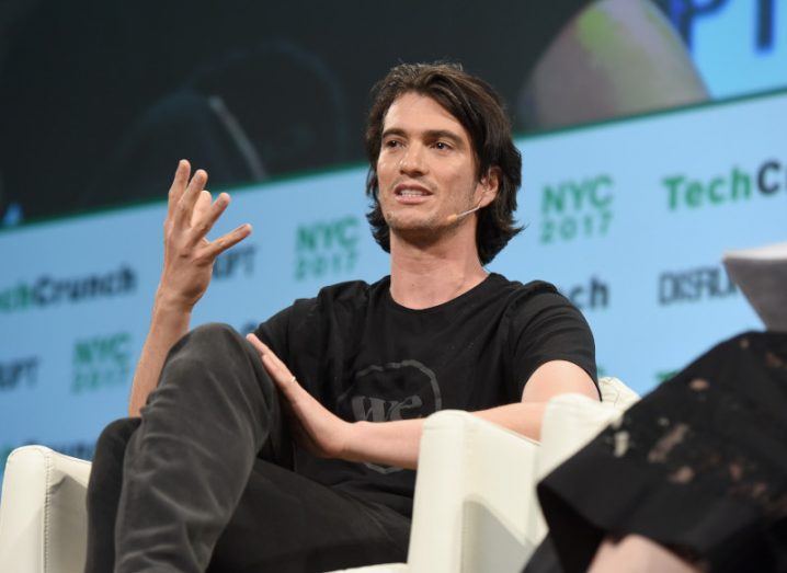 Adam Neumann seated on a stage addressing an audience.