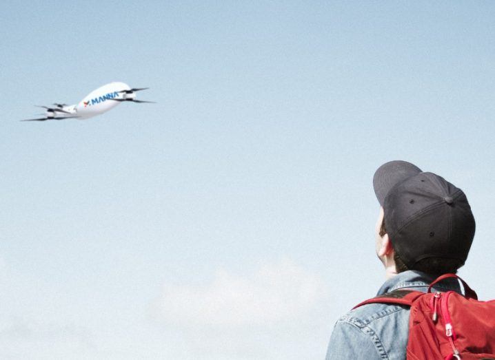 A person wearing a cap watches a Manna drone fly in the sky.