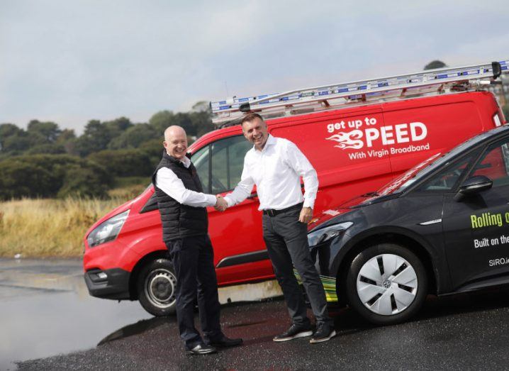 Two men shaking hands in front of a red minivan that reads "Get up to speed with Virgin Media broadband".