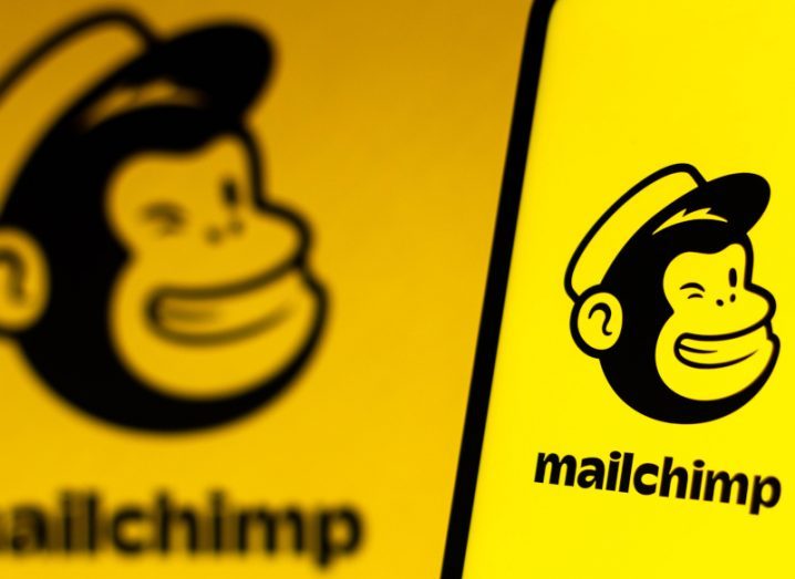 Mailchimp logo on a smartphone with another blurred logo on a screen in the background.