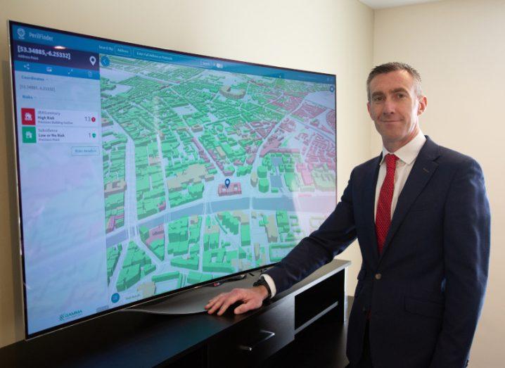 A man stands in front of a large screen TV showing a detailed map on the Perilfinder platform by Gamma.