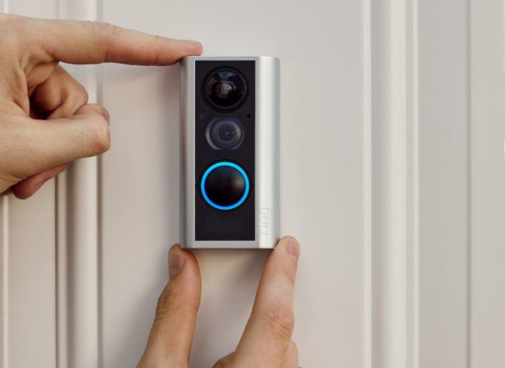 Close-up of person's hands placing an Amazon Ring doorbell device against a door.