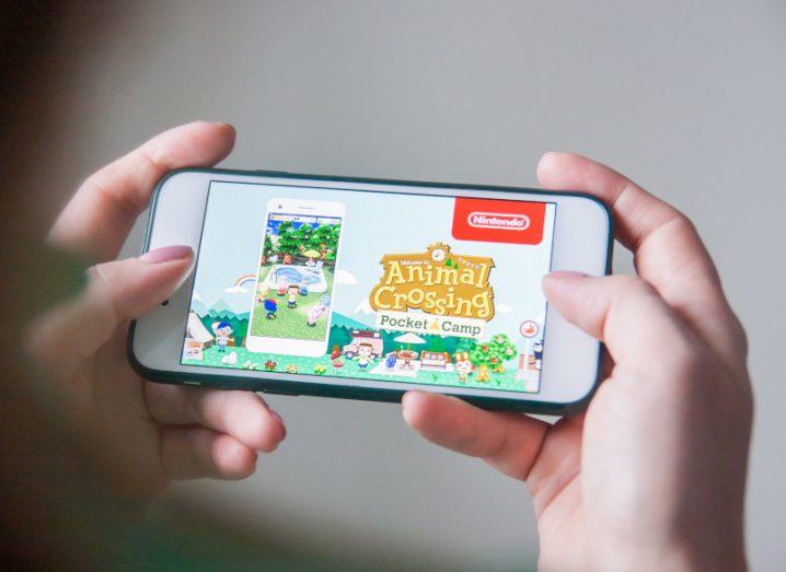 Smartphone held in a person's hands with Animal Crossing displayed on the screen.
