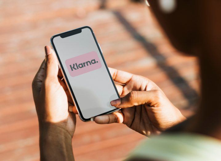Klarna app logo on a smartphone held in a person's hands.