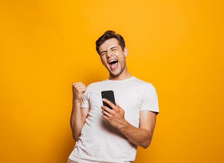Man expressing happiness while holding a smartphone in his hands. Symbolising the ability to change one's feed on Instagram.