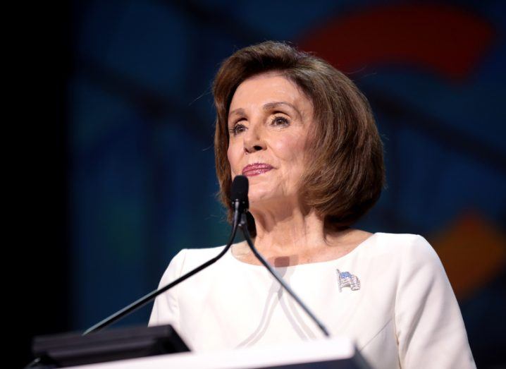 Nancy Pelosi speaking from a podium. She is wearing a brooch of the US flag.