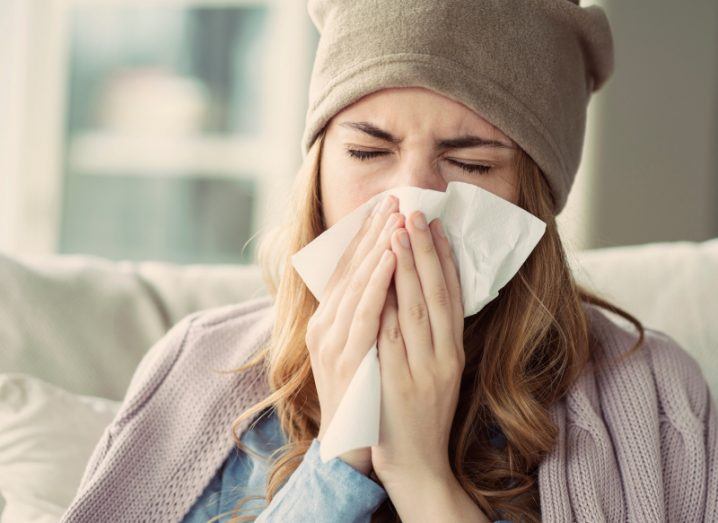 Woman sneezes into a tissue as she suffers from what appears to be influenza.