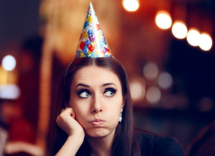 Woman wearing a party hat and sulking. Represents the Airbnb party ban.