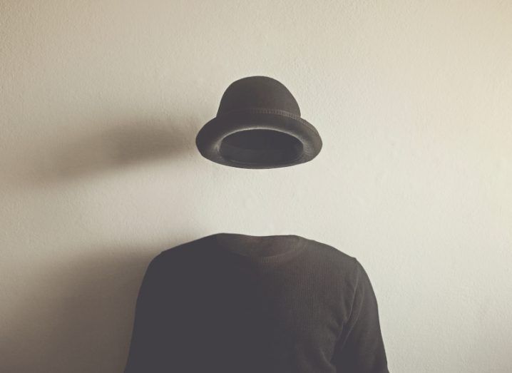 Invisible man wearing a black top and hat in front of a wall. Concept to indicate lack of identity.