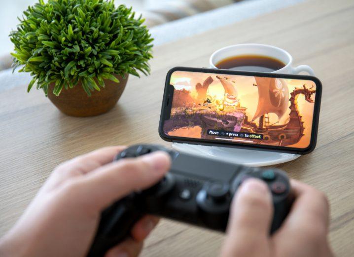 Person holding a Sony PlayStation controller and playing a game on a mobile device.