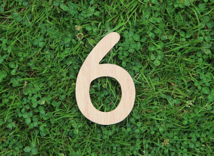 A wooden object shaped in the form of number six placed on green grass with clover.